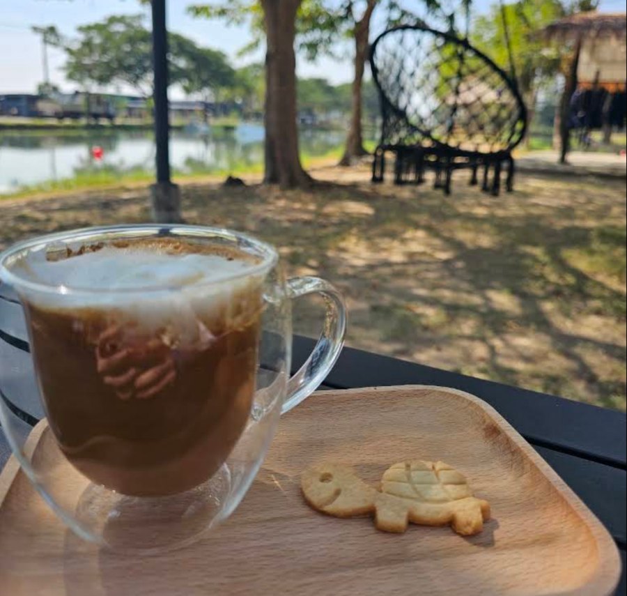 Cappuccino on a wooden tray with a turtle-shaped cookie, lake in the background